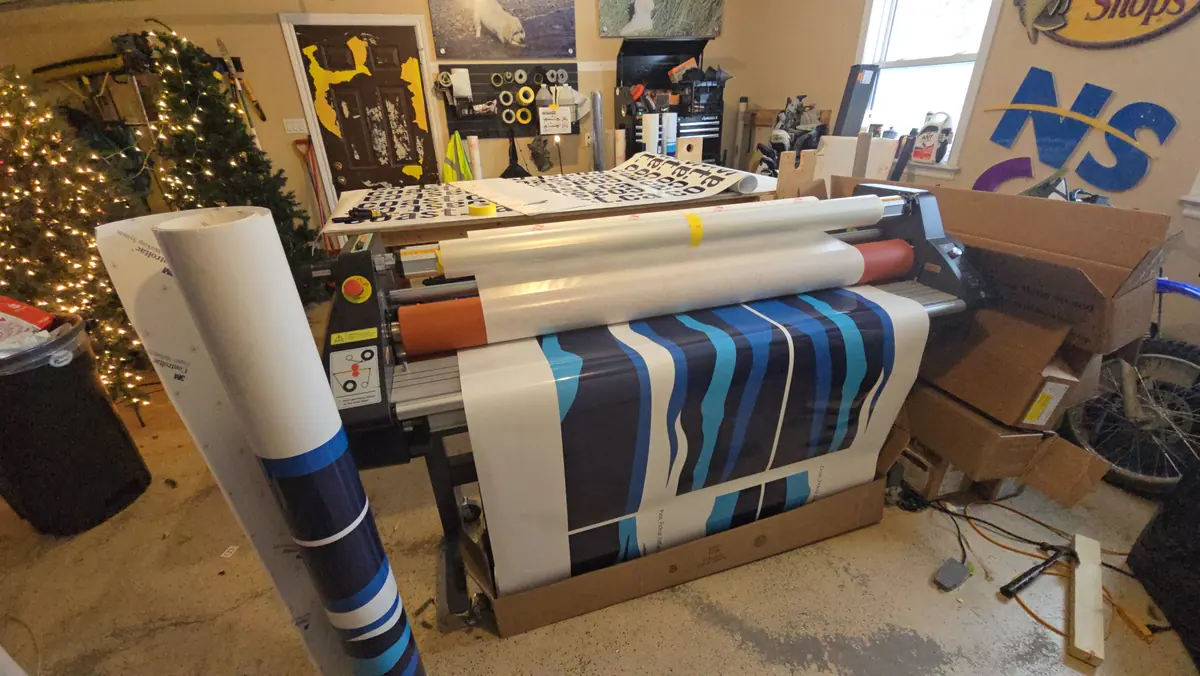 A freshly printed wrap panel running through the laminator in the ProFleet Graphics shop