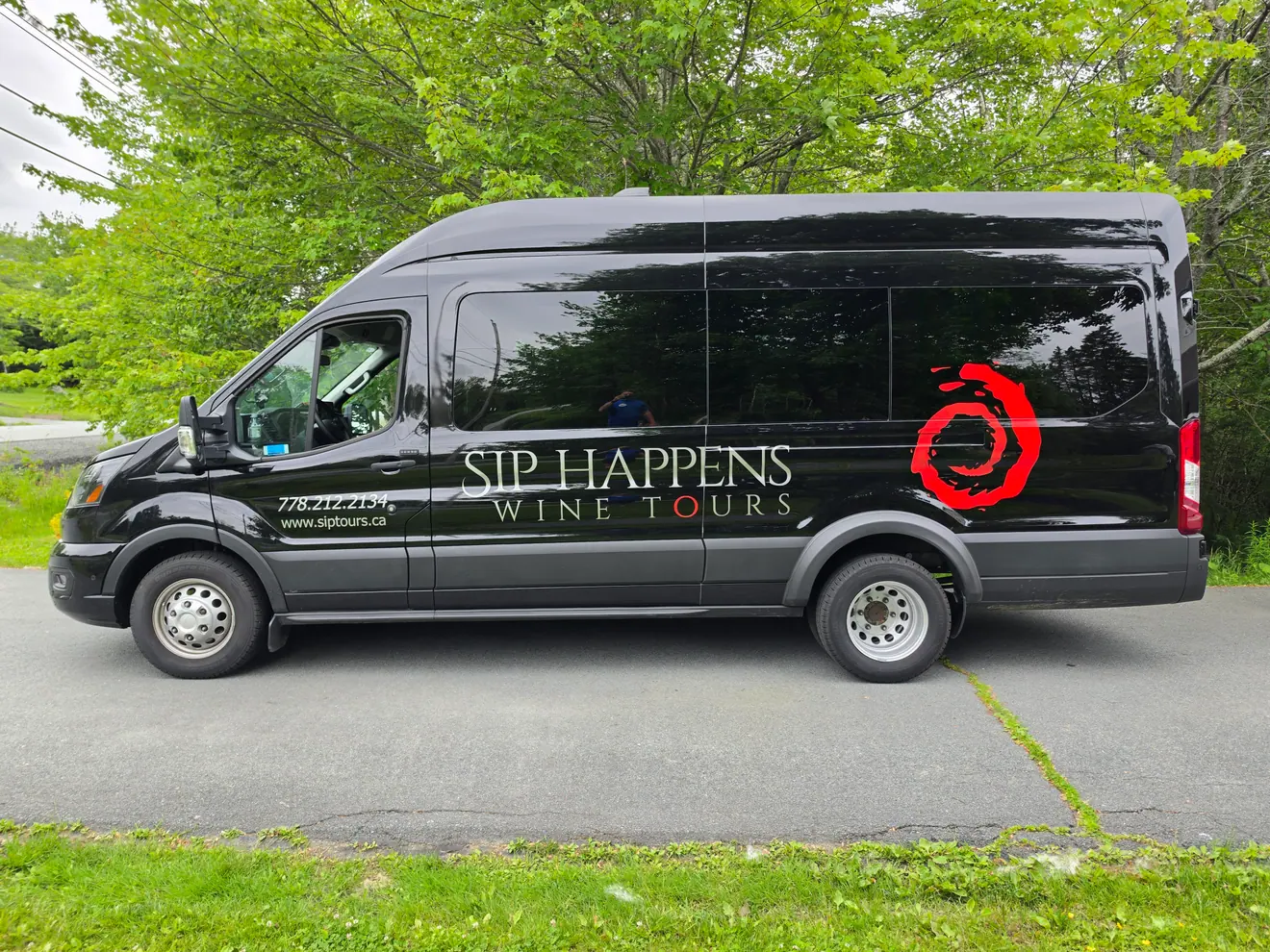 Sip Happens Wine Tours graphics on a black Ford Transit passenger van